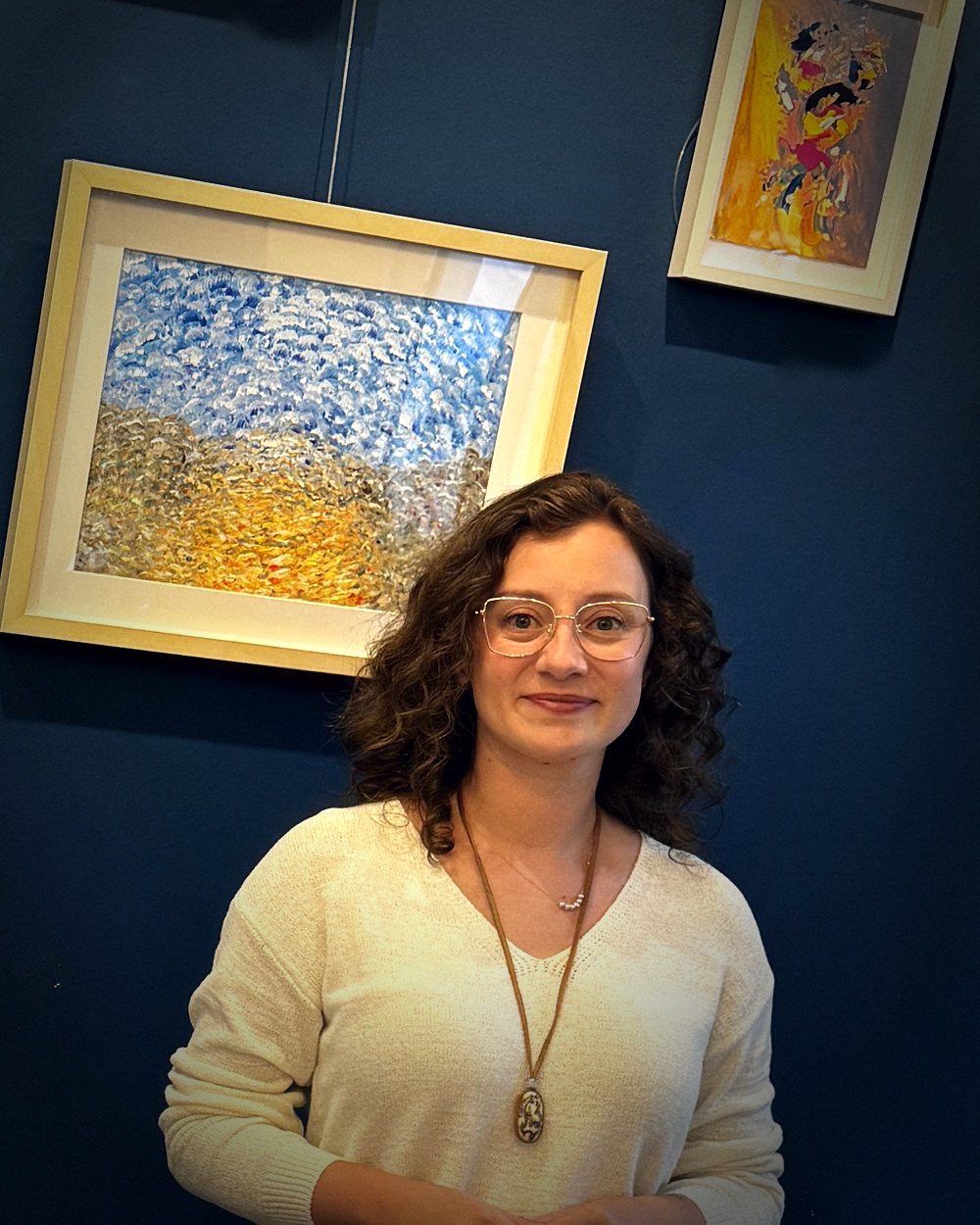Cansu Öter lächelt in einer Galerie, vor gerahmten Gemälden stehend.